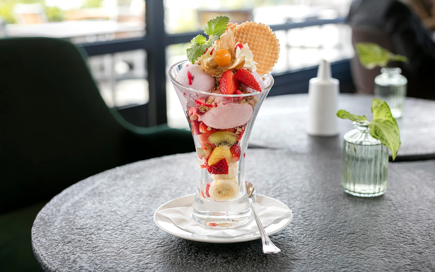 Ein bunter Eisbecher mit frischen Früchten und Waffel auf einem Tisch.