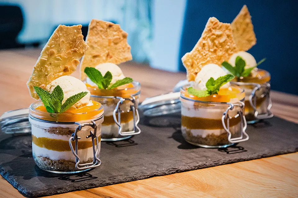 Vier Gläser mit Dessert, Schichten aus Joghurt, Karamell und Eis, dekoriert mit Minze.