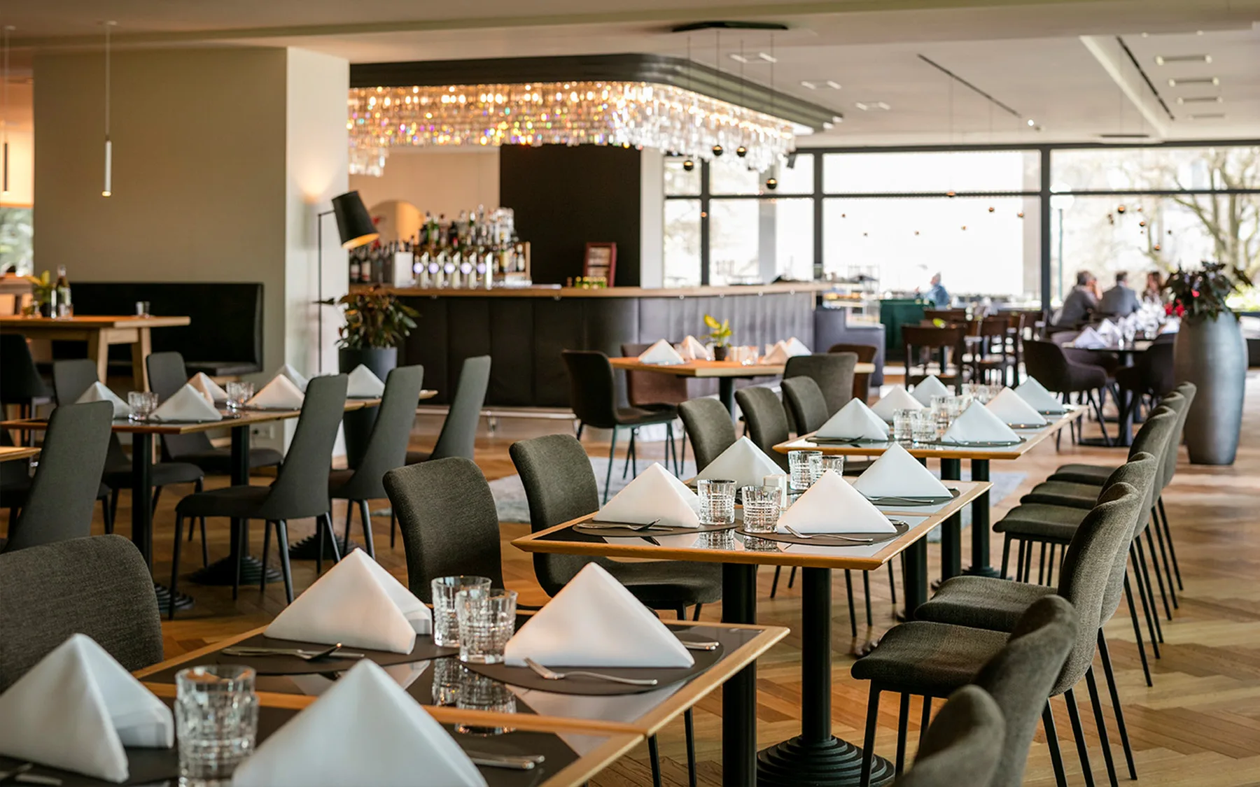 Innenansicht eines eleganten Restaurants mit gedeckten Tischen und einer Bar im Hintergrund.