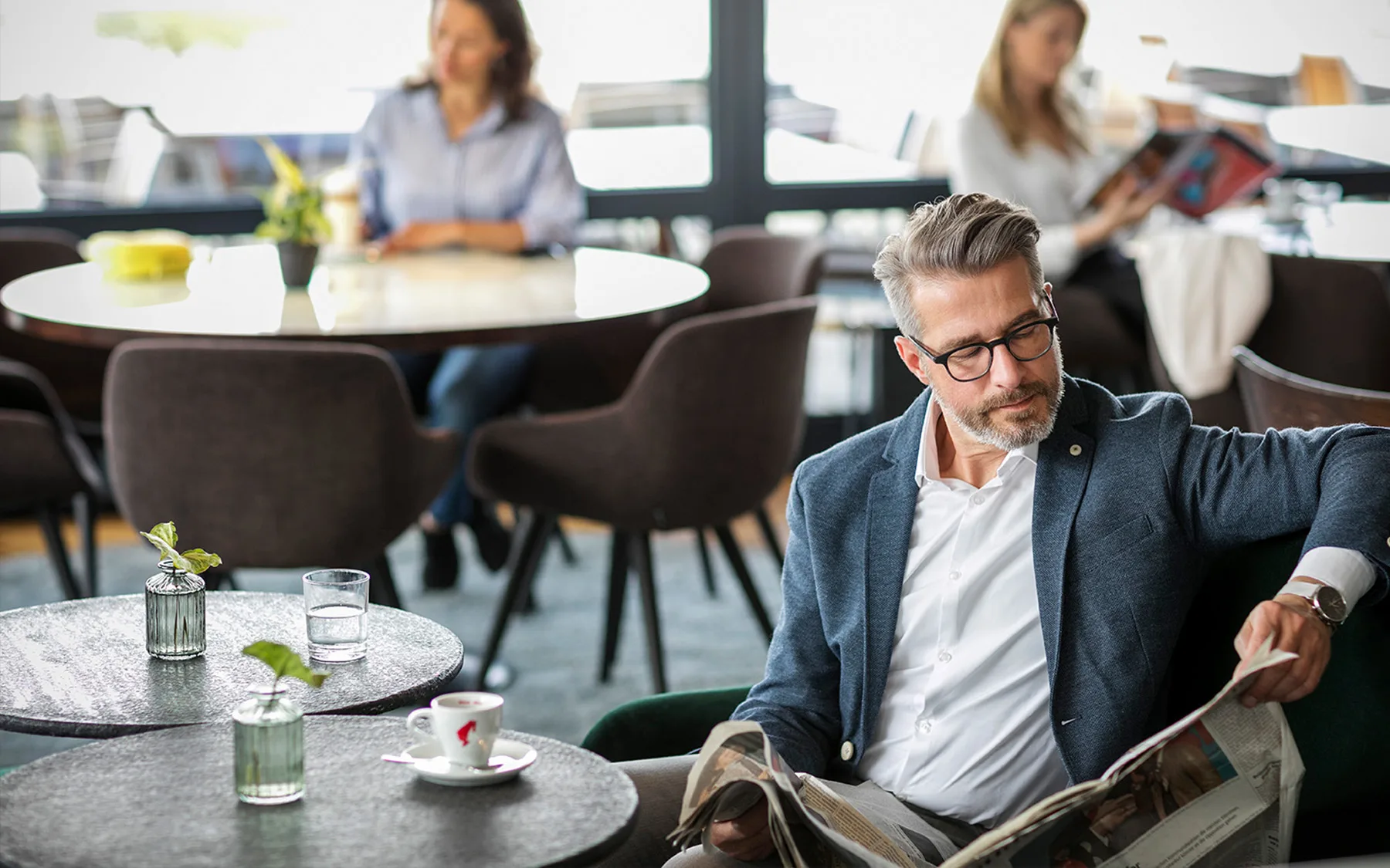 Ein Mann sitzt in einem modernen Café und liest eine Zeitung.
