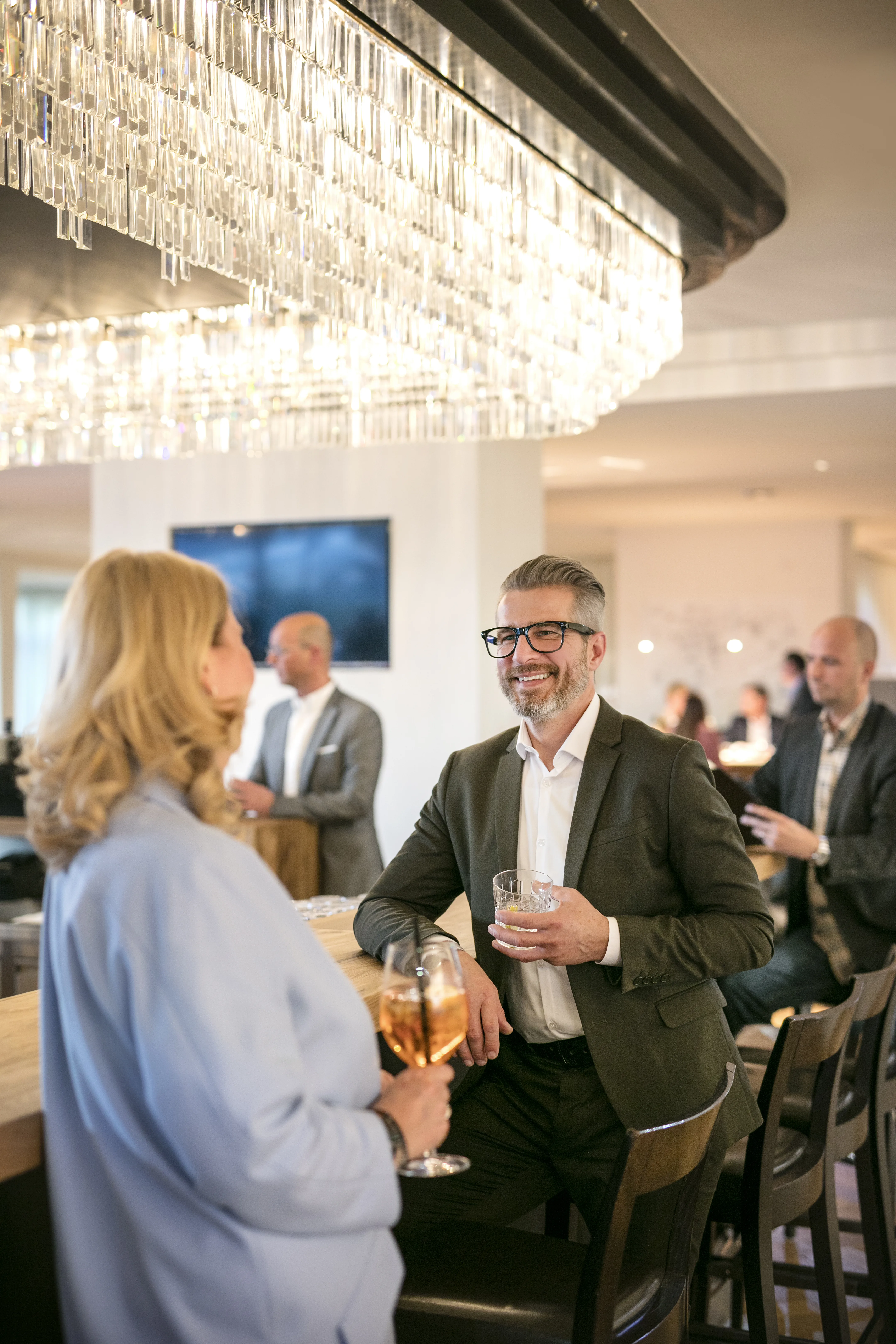 Zwei Personen unterhalten sich an einer Bar mit Gläsern in der Hand.